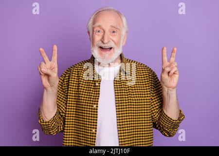 Photo portrait of optimistic granddad grey hair double v-sign wear stylish yellow checkered shirt isolated on lilac violet color background Stock Photo