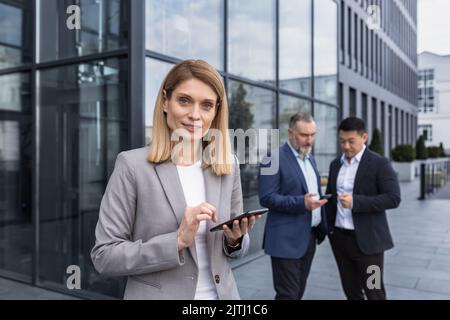 Portrait of successful senior woman businessman and specialist, program manager with tablet computer outside office building smiling and looking at camera, professional programmer team leader. Stock Photo