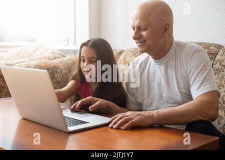 Grandfather and granddaughter spend time together use laptop, browse website, younger generation teach explain to older how to use modern tech concept Stock Photo