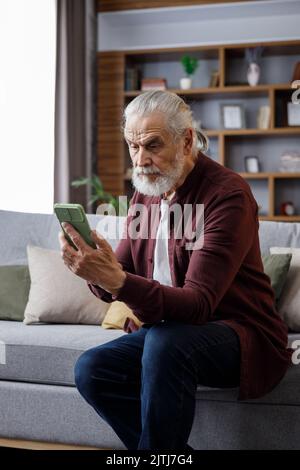 Smiling elderly gray-haired man using smartphone for texting message, playing video games, watching video. Hobby,leisure,entertainment. Active senior Stock Photo
