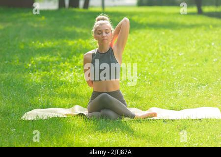 A slender woman sitting on mat in the park, performing yoga Stock Photo