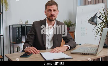 Stressed businessman in formal wear suit feeling worried about financial problem doing paperwork at office. Concentrated male freelancer man frustrated thinking of money debt, budget loss, bankruptcy Stock Photo