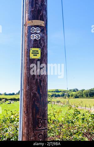 Sign on a wooden telephone pole warning people that the pole is carrying fibre optic cable. Stock Photo