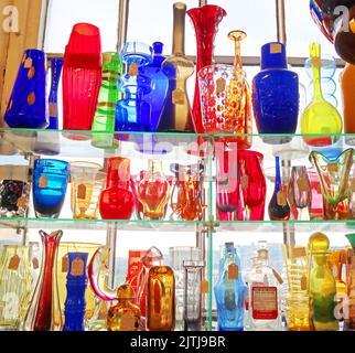 Vintage coloured mixed glassware in window shelf, lighted Stock Photo