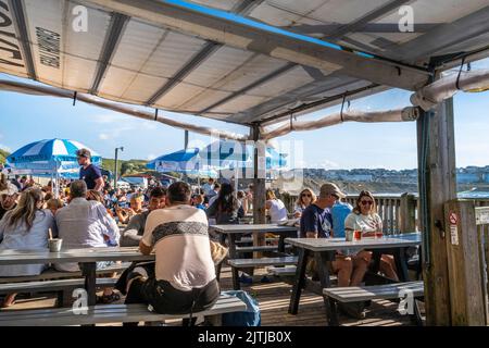 Holidaymakers relaxing on the outdoor seating area of the popular Fistral Beach Bar in Newquay in Cornwall in the UK. Stock Photo
