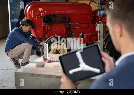 31 August 2022, Lower Saxony, Osnabrück: An industrial computer scientist scans an axle stub from a Porsche Junior 108 tractor for illustration purposes using a tablet and software that relies on artificial intelligence. Industrial engineer Tobias Dreesbach (back) from the German Research Center for Artificial Intelligence (DFKI) looks through augmented reality (AR) glasses. In the future, the Research Center for Artificial Intelligence (DFKI) and the Museum of Industrial Culture (MIK) want to work together to prepare formats for a broad audience. The focus will be on industrial history and cu Stock Photo