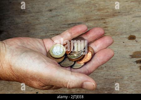 An elderly hand hold a few pounds worth of British coinage. How far will it stretch. Stock Photo