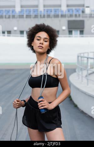 Portrait of african american sportswoman holding jump rope and looking at camera on stadium Stock Photo