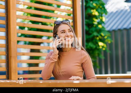 Young charming woman calls on a mobile phone while sitting in a cafe in her free time, an attractive woman with a sweet smile talks on a mobile phone Stock Photo