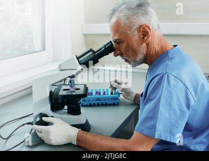 Professional male scientist looking in microscope while working on medical blood research in science medical lab Stock Photo