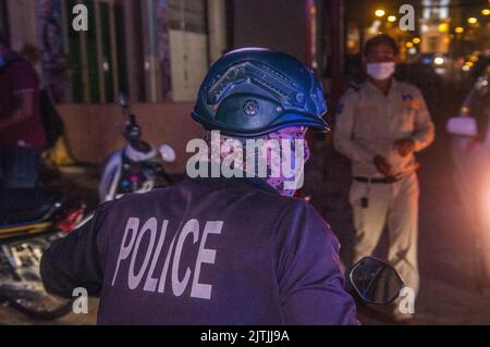 during an outbreak of COVID - 19, a Cambodian policeman in a camouflage protective face mask / covering gets ready to leave the scene of an ambulance picking up a woman w/ coronavirus. March 14th, 2021. Stueng Meanchey, Phnom Penh, Cambodia. © Kraig Lieb Stock Photo