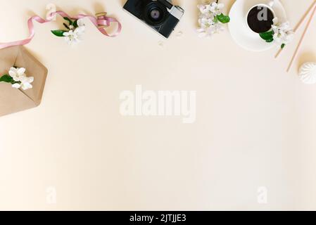 Flat female home office desk for ladies. Workspace with retro camera, coffee cup and apple blossoms on beige background with copy space Stock Photo