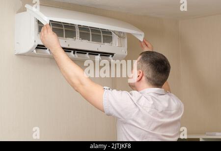 A man fixes the air conditioner, cleans the filters from dust, checks the performance Stock Photo