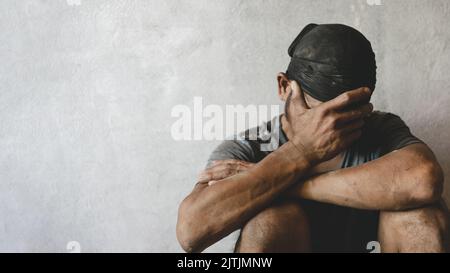 Man suffering from depression, Homeless man drug and alcohol addict sitting alone and depressed on the street feeling anxious and lonely, social docum Stock Photo