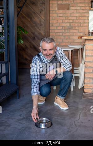 Kind-hearted coffee shop owner feeding a pet in his establishment Stock Photo