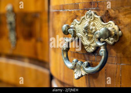 Decorative metal drawer handle in an antique desk with inlaid wood, Mid-18th century, close up. Stock Photo