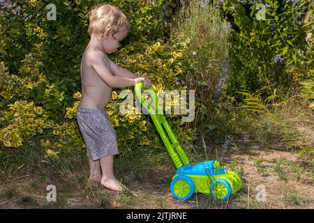 A little boy pushes a lawnmower blowing bubbles in the garden Stock Photo