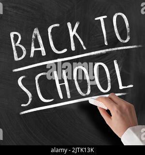 hand of teacher holding piece of chalk against chalkboard with text BACK TO SCHOOL Stock Photo