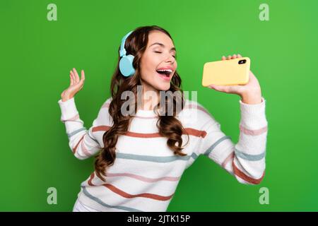 Photo of pretty funky lady wear striped sweater earphones singing songs modern device isolated green color background Stock Photo