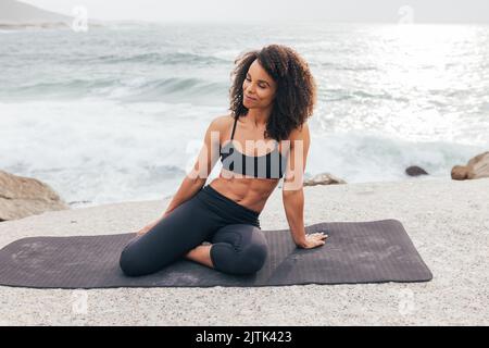 Smiling woman in fitness wear sitting on mat with closed eyes by bay Stock Photo