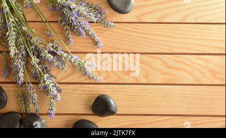 Wellness concept with black stonesand and spikes of flowering lavender on wooden table. Top view. Stock Photo