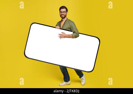 Happy middle aged man carrying big smartphone with empty white screen, walking with gadget under arm, mockup Stock Photo