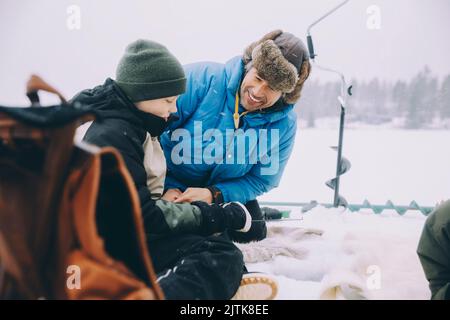 Happy father talking with son sitting on frozen lake Stock Photo