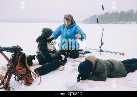 Happy man talking with son while friend fishing lying on snow Stock Photo