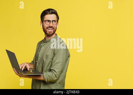 Remote job concept. Happy man with laptop in hands looking aside at copy space, standing on yellow background Stock Photo