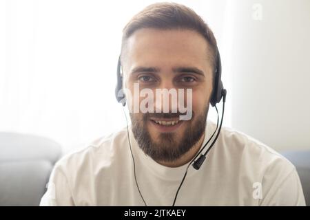 Head shot portrait man wearing glasses and headphones speaking at camera, making video call, using webcam, engaged in online conference at home Stock Photo