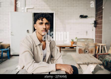 Portrait of young man sitting at table in front of wall Stock Photo