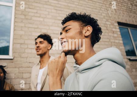 Smiling man with hand on chin standing by friend outside building Stock Photo