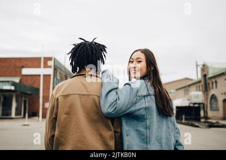 Smiling woman looking over shoulder while walking with friend on street Stock Photo