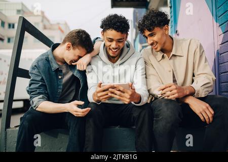 Happy man using smart phone while sitting with friends outdoors Stock Photo