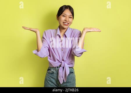 Asian Lady Shrugging Shoulders Smiling To Camera Over Yellow Background Stock Photo