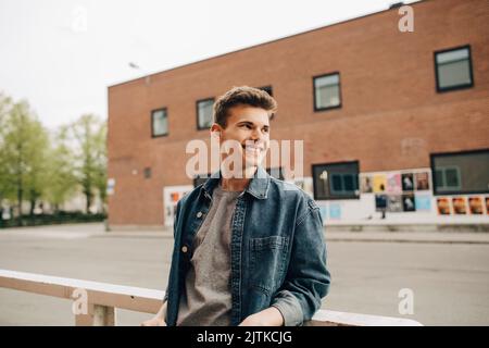 Smiling young man looking away while leaning on railing Stock Photo