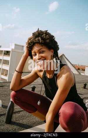 Portrait of happy young woman crouching on rooftop during sunny day Stock Photo