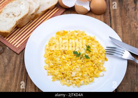 fresh scrambled eggs on white plate on breakfast table Stock Photo