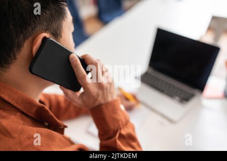 Unrecognizable Japanese Businessman Talking On Phone Using Laptop At Workplace Stock Photo