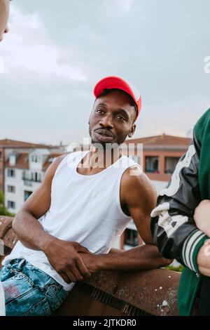 Young man wearing hat talking with male friend on rooftop Stock Photo