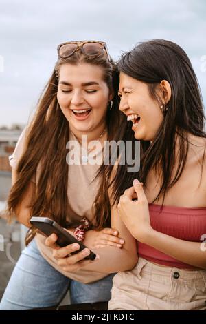 Young women laughing while sharing smart phone Stock Photo