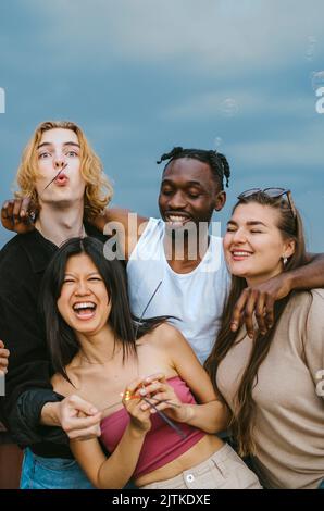 Happy multiracial male and female friends having fun together against sky Stock Photo