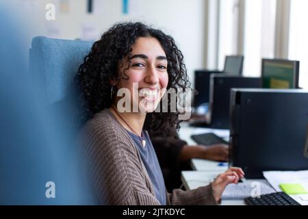 Side view of happy businesswoman sitting at desk in office Stock Photo