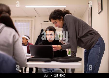 Teacher leaning on desk assisting student using laptop in classroom Stock Photo