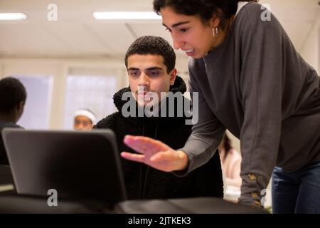 Student looking at laptop while teacher explaining in classroom Stock Photo