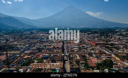 Beautiful aerial cinematic footage of the Antigua City in Guatemala, Its yellow church, the Santa Catalina Arch and the Acatenango Volcano Stock Photo