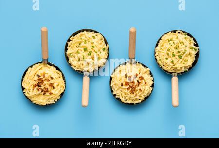 Above view with small pans of spaetzle on a blue table. German dish, pasta with cheese and onion. Delicious bavarian cheese noodles. Stock Photo