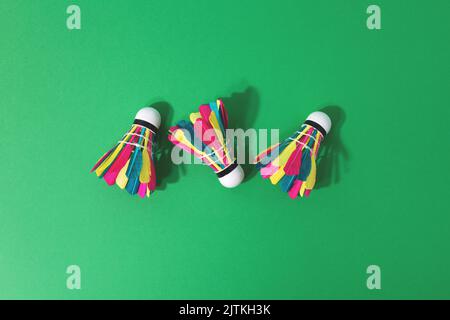 Top view of three feathered colourful shuttlecocks on green background with copy space. Summer activity concept. Studio shot, hard light. Stock Photo