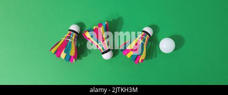 Colourful shuttlecocks and white ball on green background. Badminton, summer activity. Banner 16:6 Stock Photo