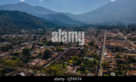 Beautiful aerial cinematic footage of the Antigua City in Guatemala, Its yellow church, the Santa Catalina Arch and the Acatenango Volcano Stock Photo